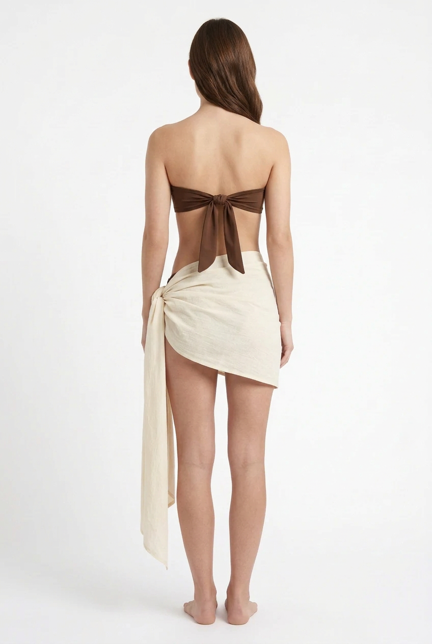 Vista posterior de modelo con PAREO 22’ color crema anudado al costado y top de bikini café.