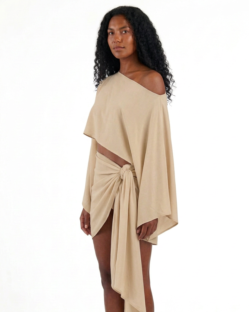 Conjunto ZAMNA beige de MIZZBOGI sobre modelo, vista lateral del top asimétrico y pareo con amarre lateral.
